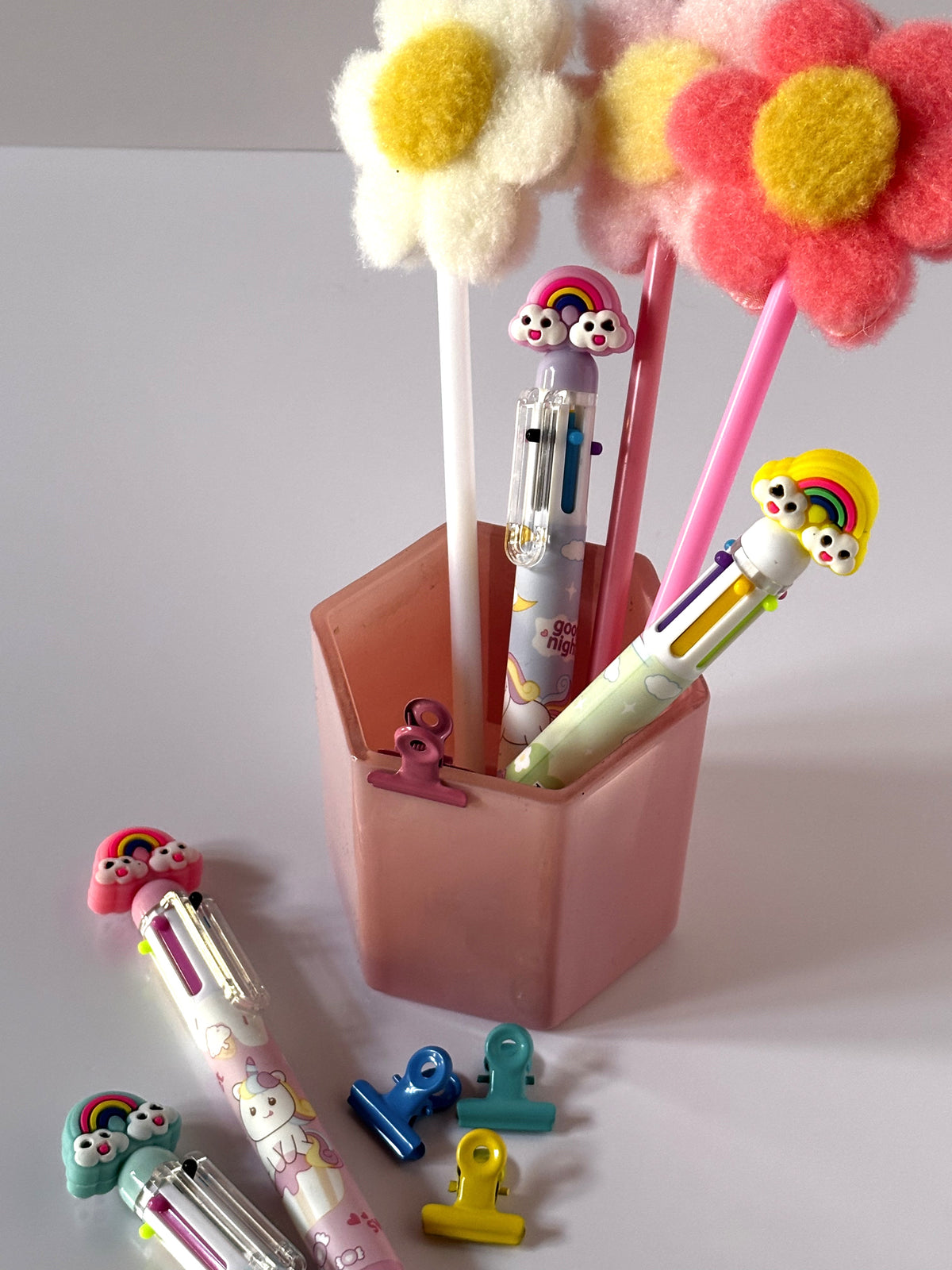 Set completo di quattro penne multicolore Kawaii con fusti assortiti nei colori rosa, lilla, celeste e bianco, dotate di topper 3D ad arcobaleno e grafiche di unicorni.