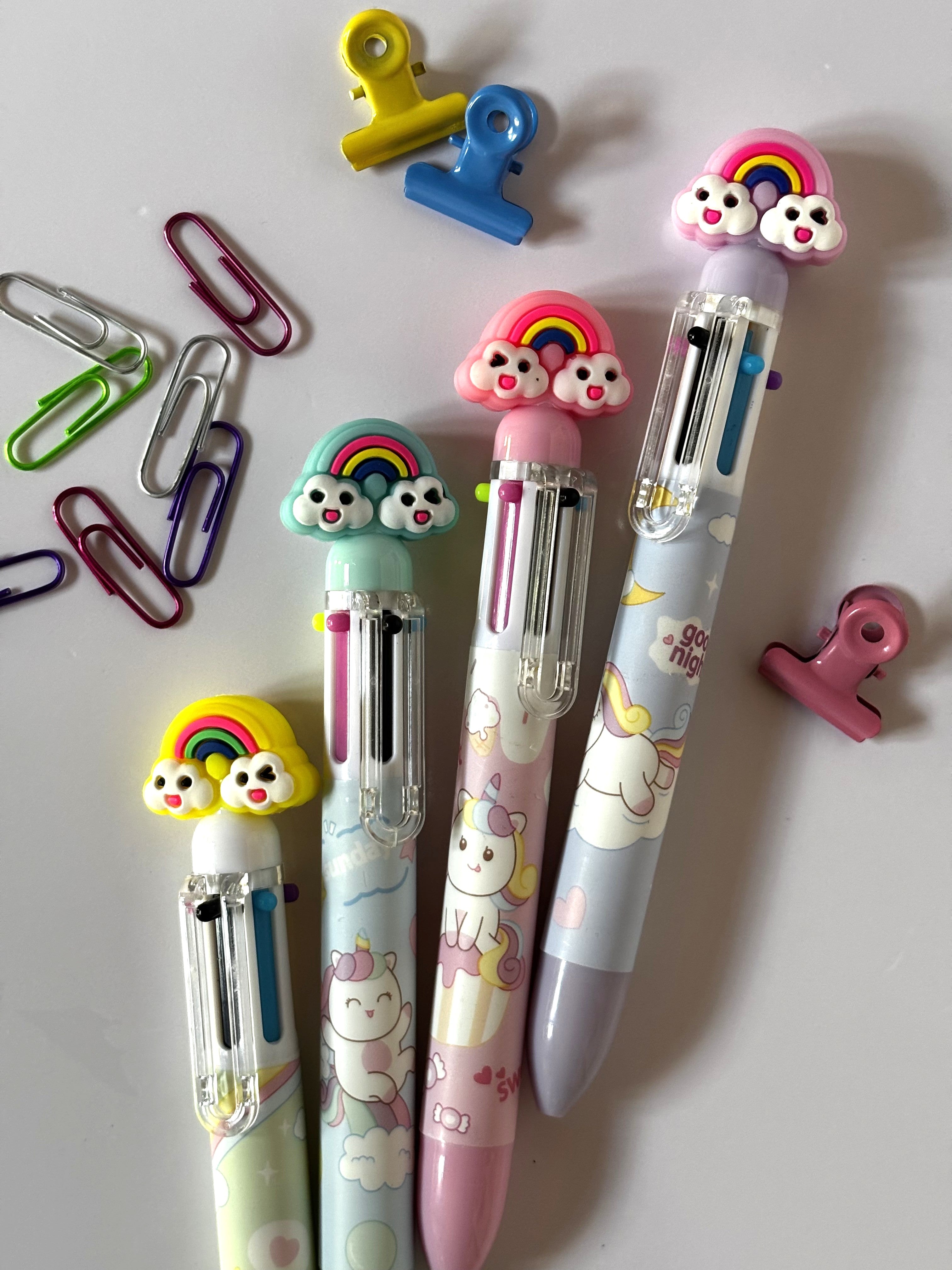Set completo di quattro penne multicolore Kawaii con fusti assortiti nei colori rosa, lilla, celeste e bianco, dotate di topper 3D ad arcobaleno e grafiche di unicorni.