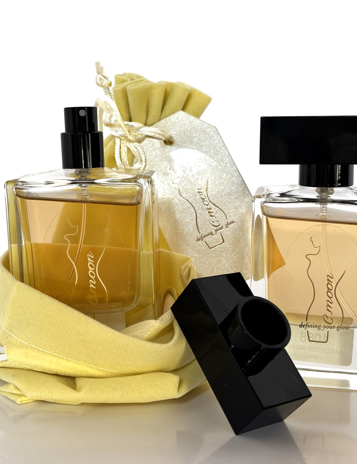 Flaconi di profumo C.Moon "Defining Your Glow" da 50ml in vetro con silhouette dorata, completi di sacchetto in tessuto giallo pastello e tag regalo coordinato.