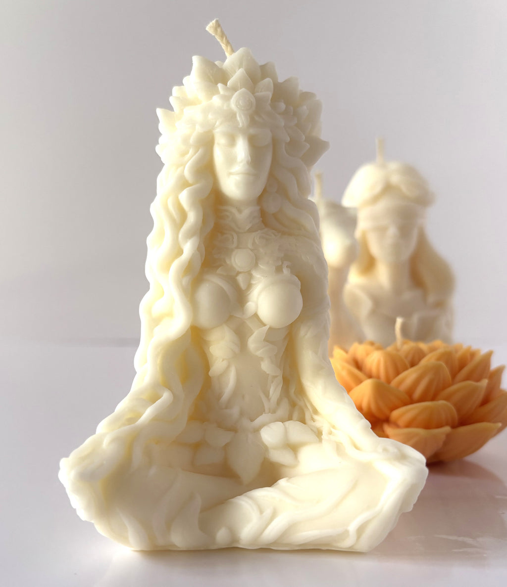 Candela scultorea C.Moon color bianco avorio raffigurante la Dea Gaia in meditazione con foglie intrecciate nei capelli, con candela a fiore di loto sfocata sulla destra.
