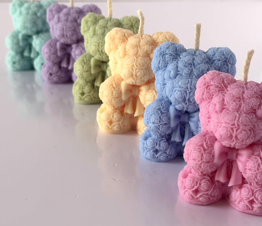 Una fila prospettica di candele C.Moon a forma di orsetto fatti di roselline con fiocco nei colori rosa, azzurro, giallo, verde, lilla e menta.