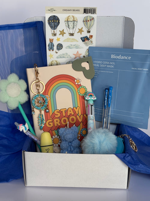 Cofanetto regalo Good Vibes C.Moon da 59.90€ in variante azzurra, contenente un quaderno con la scritta Stay Groovy e un arcobaleno freddo, una candela azzurra a forma di orsetto, una maschera Biodance idratante blu, un portachiavi dorato acchiappasogni, uno specchietto azzurro con pompon e stickers con mongolfiere.
